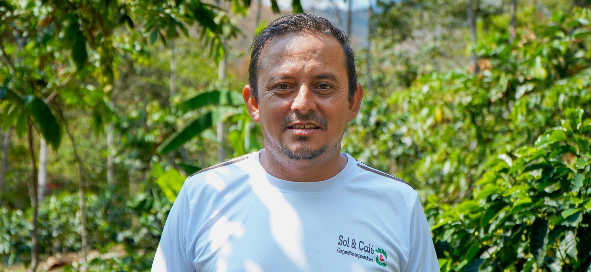 Marbin Asunción Villegas standing among coffee plants on his farm, wearing a Sol & Café shirt.